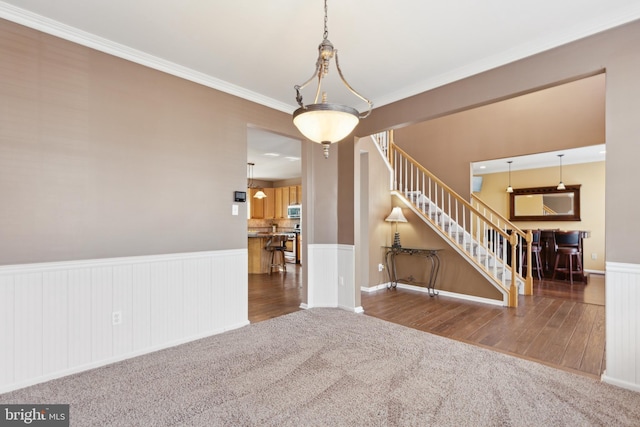 empty room featuring dark wood-style flooring, a wainscoted wall, dark colored carpet, stairway, and ornamental molding