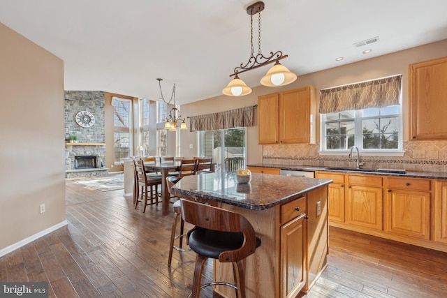 kitchen featuring light wood finished floors, tasteful backsplash, visible vents, a kitchen island, and a sink