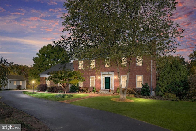 view of front of property featuring driveway, brick siding, and a yard