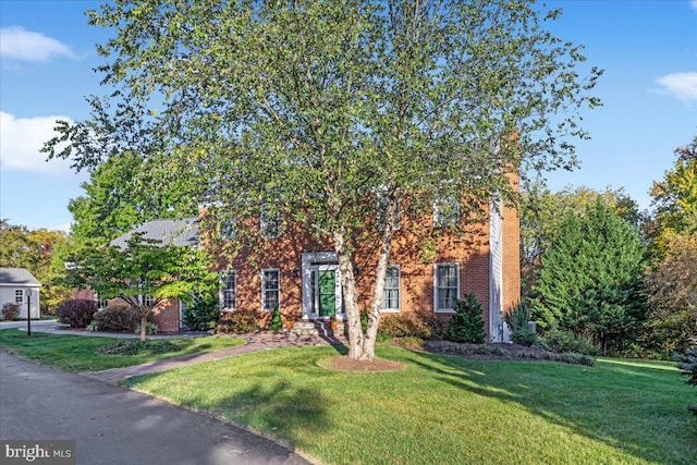 view of property hidden behind natural elements featuring a front lawn and brick siding