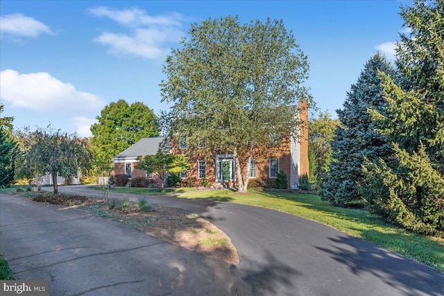 view of front facade featuring brick siding, a chimney, and a front yard