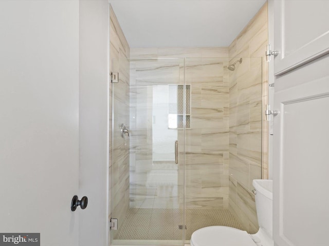 bathroom featuring a shower with door and toilet