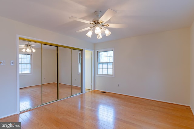 unfurnished bedroom with ceiling fan, a closet, light hardwood / wood-style floors, and multiple windows