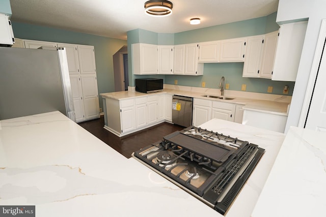 kitchen with white cabinetry, stainless steel appliances, sink, and light stone counters