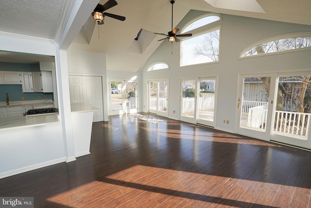 unfurnished living room with dark wood-type flooring, sink, high vaulted ceiling, a textured ceiling, and ceiling fan