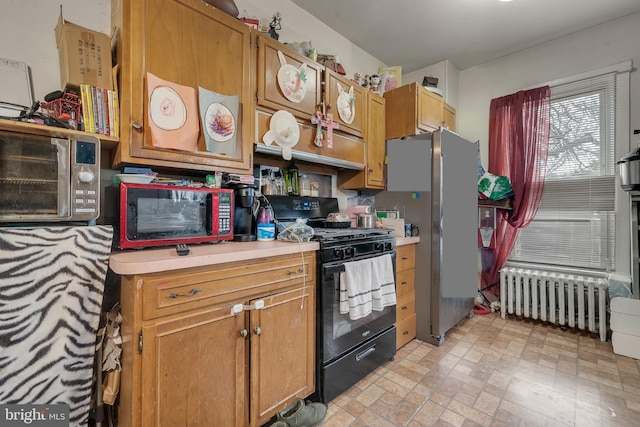 kitchen featuring radiator heating unit, stainless steel refrigerator, and black gas stove