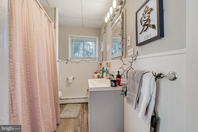 bathroom featuring hardwood / wood-style flooring, baseboard heating, vanity, a drop ceiling, and toilet