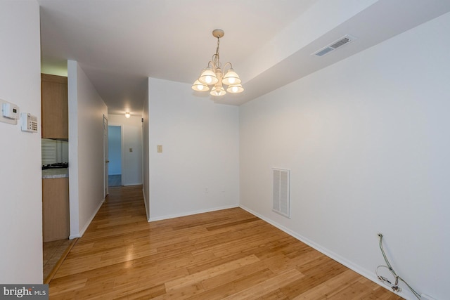 unfurnished dining area featuring an inviting chandelier and light hardwood / wood-style floors