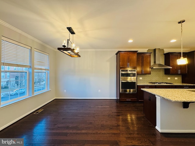 kitchen featuring crown molding, a breakfast bar, hanging light fixtures, stainless steel appliances, and wall chimney exhaust hood