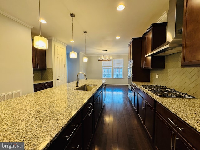 kitchen with pendant lighting, sink, backsplash, light stone countertops, and wall chimney exhaust hood