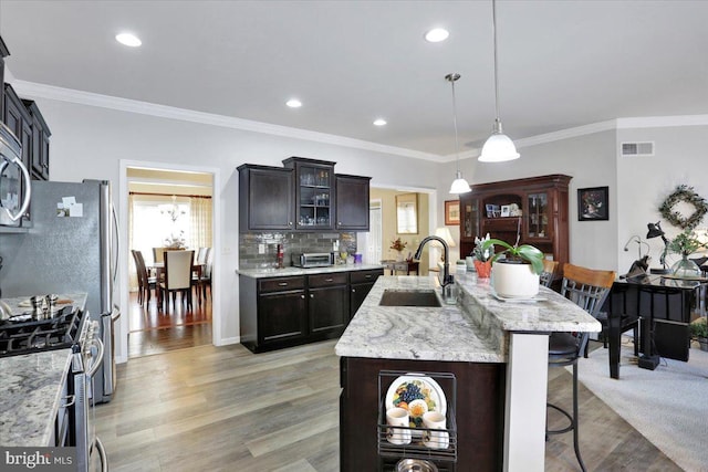 kitchen featuring a center island with sink, decorative light fixtures, light hardwood / wood-style flooring, a breakfast bar, and sink