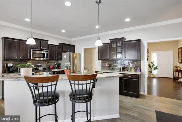 kitchen featuring appliances with stainless steel finishes, pendant lighting, backsplash, and a kitchen island with sink