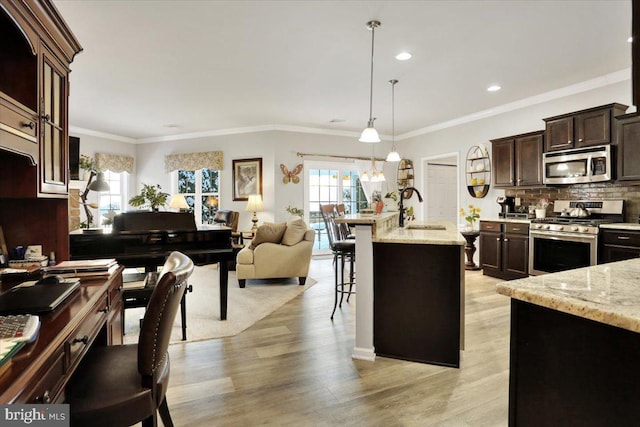 kitchen with light stone countertops, appliances with stainless steel finishes, decorative light fixtures, a kitchen breakfast bar, and sink