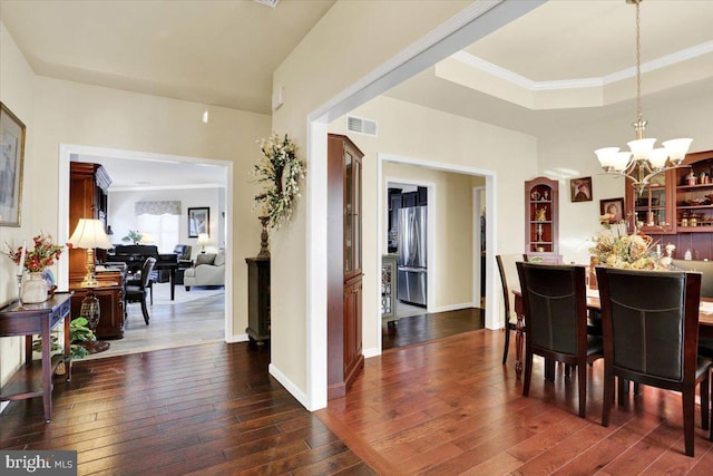 dining area featuring a raised ceiling, dark wood-type flooring, crown molding, and a chandelier