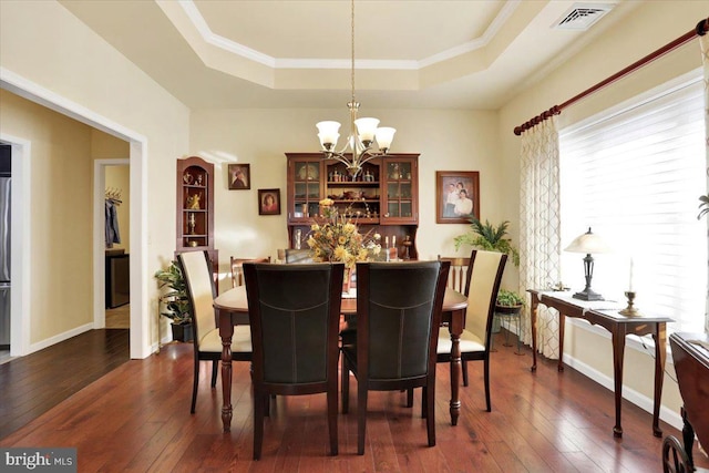 dining room featuring dark wood-type flooring, a chandelier, crown molding, and a raised ceiling