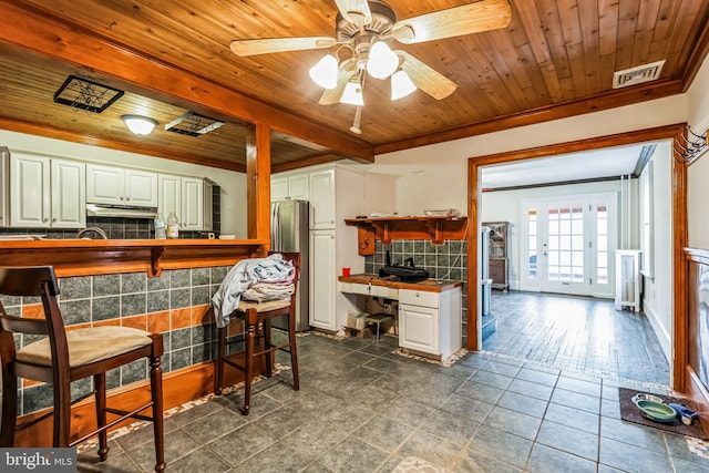 kitchen featuring wood ceiling, tile countertops, stainless steel refrigerator, decorative backsplash, and white cabinets