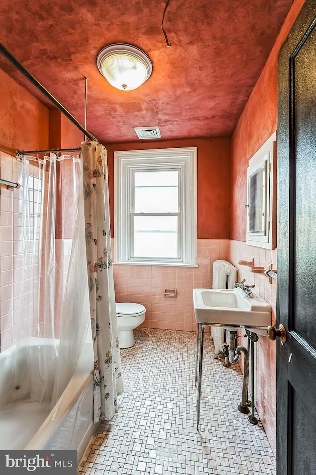 bathroom with tile walls, tile patterned floors, toilet, and shower / bath combo with shower curtain