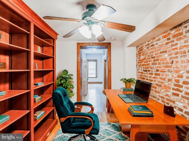 home office featuring ceiling fan, brick wall, and light hardwood / wood-style floors