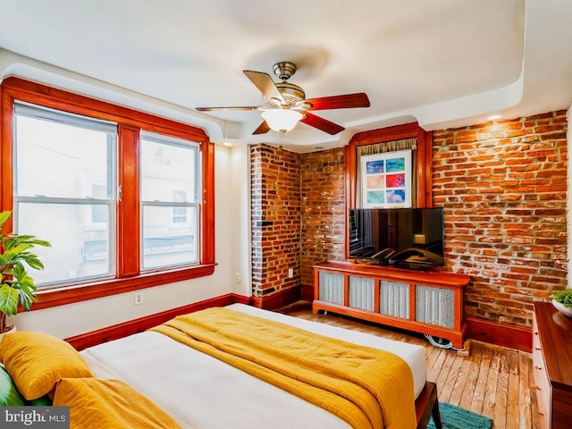 bedroom with wood-type flooring, brick wall, radiator, and ceiling fan