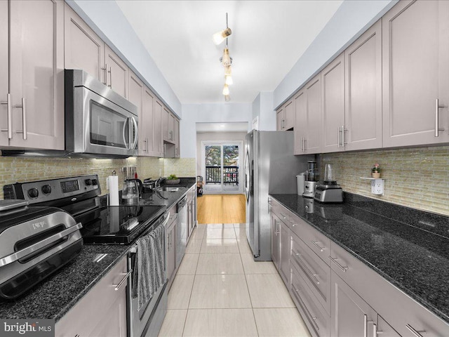 kitchen with light tile patterned floors, gray cabinets, appliances with stainless steel finishes, backsplash, and dark stone countertops