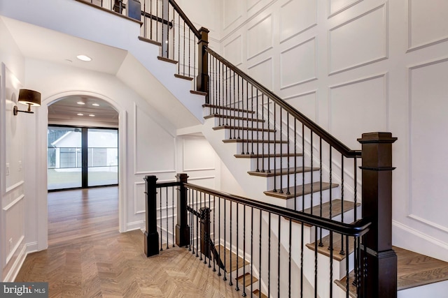 stairway with a towering ceiling, arched walkways, a decorative wall, and recessed lighting