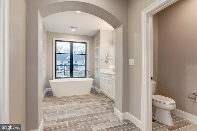 bathroom with wood finish floors, visible vents, a freestanding bath, and toilet