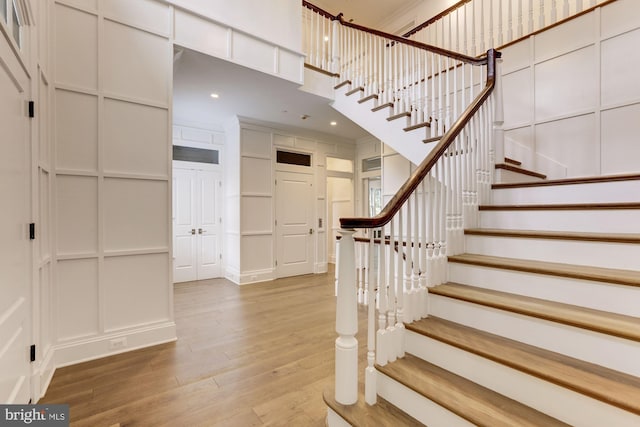 stairs with a high ceiling, recessed lighting, wood finished floors, and a decorative wall