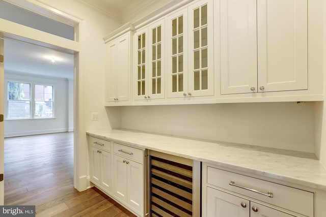 bar featuring wine cooler, baseboards, ornamental molding, light wood-type flooring, and a bar