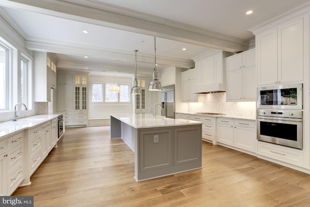 kitchen featuring white cabinetry, a center island with sink, hanging light fixtures, and built in appliances