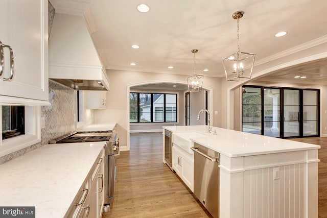 kitchen featuring light stone counters, hanging light fixtures, appliances with stainless steel finishes, a sink, and premium range hood