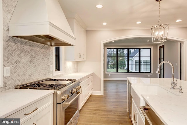 kitchen featuring light stone counters, white cabinets, high end range, decorative light fixtures, and custom range hood