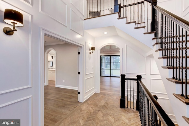 corridor featuring arched walkways, a decorative wall, a high ceiling, baseboards, and parquet floors