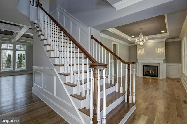 staircase featuring a fireplace with flush hearth, ornamental molding, wood finished floors, a decorative wall, and a notable chandelier