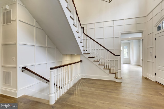 stairs with high vaulted ceiling, visible vents, a decorative wall, and wood finished floors