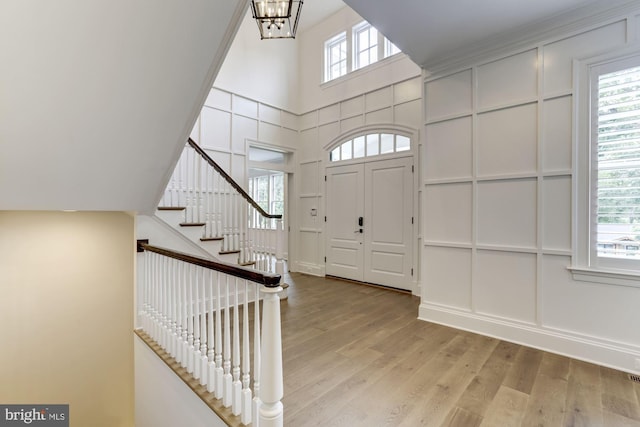 entrance foyer featuring a towering ceiling, stairway, light wood-type flooring, a chandelier, and a decorative wall