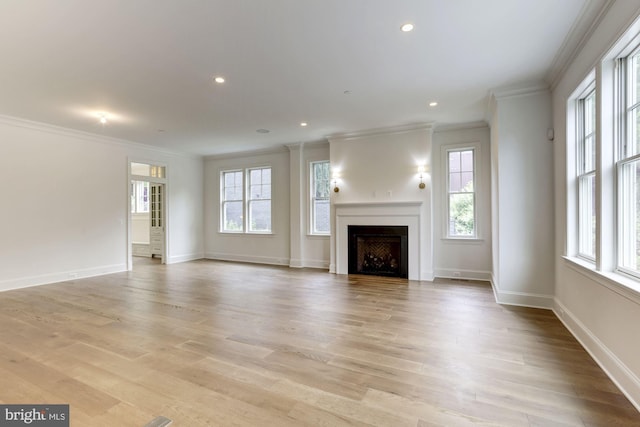 unfurnished living room with light wood finished floors, a fireplace, ornamental molding, and a wealth of natural light