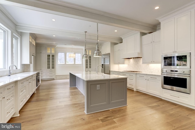 kitchen featuring built in appliances, an island with sink, white cabinets, and pendant lighting