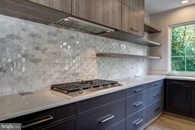 kitchen with stainless steel gas cooktop, light wood finished floors, open shelves, decorative backsplash, and premium range hood