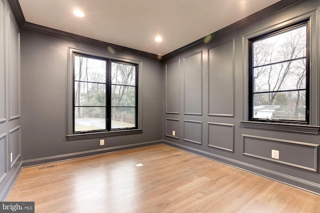 empty room with visible vents, crown molding, light wood-style floors, a decorative wall, and recessed lighting