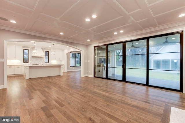 unfurnished living room with light wood-style floors, crown molding, arched walkways, and a wealth of natural light