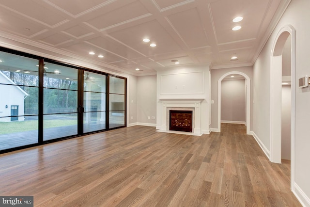 unfurnished living room featuring arched walkways, crown molding, a fireplace with flush hearth, light wood-style floors, and baseboards