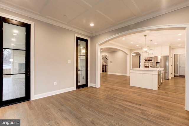 unfurnished living room featuring arched walkways, light wood finished floors, ornamental molding, and baseboards