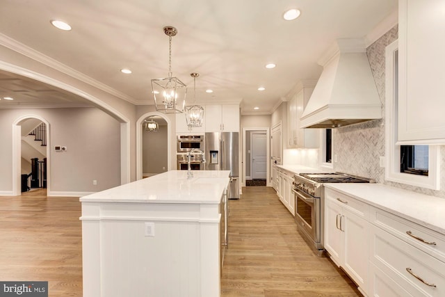 kitchen with stainless steel appliances, arched walkways, a kitchen island with sink, and custom range hood