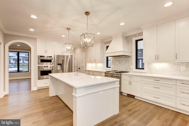 kitchen featuring high quality appliances, white cabinets, light countertops, custom exhaust hood, and a center island with sink