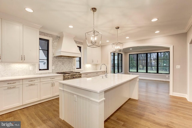 kitchen featuring light countertops, premium range hood, an island with sink, and high end stainless steel range oven