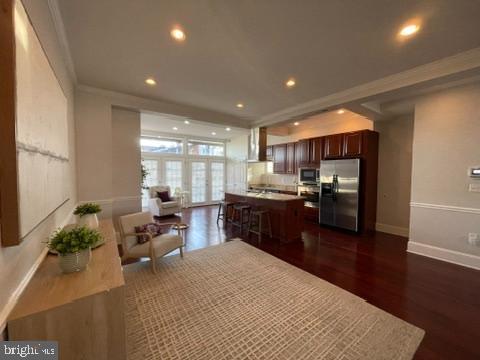 kitchen with wall chimney range hood, appliances with stainless steel finishes, dark hardwood / wood-style floors, a center island, and ornamental molding