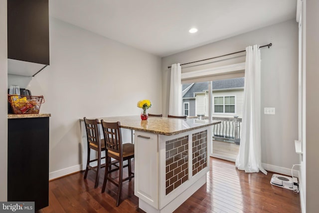 kitchen with a breakfast bar area, white cabinets, light stone counters, kitchen peninsula, and dark wood-type flooring