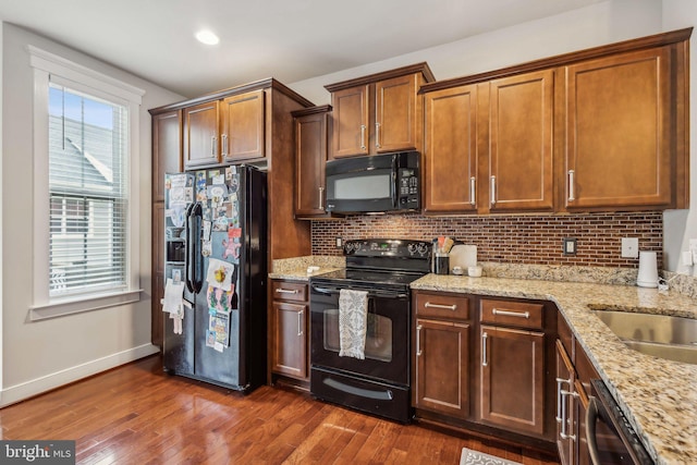 kitchen featuring dark hardwood / wood-style floors, tasteful backsplash, sink, light stone counters, and black appliances