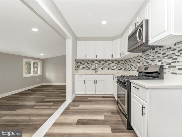 kitchen with light hardwood / wood-style floors, backsplash, white cabinetry, and stainless steel appliances