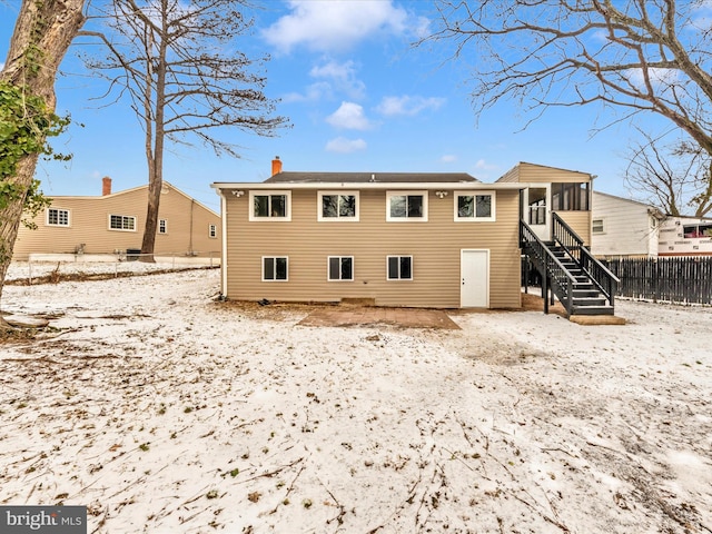 snow covered back of property with a sunroom